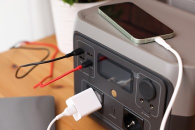 Photo of Devices charging from portable power station on wooden desk indoors, closeup