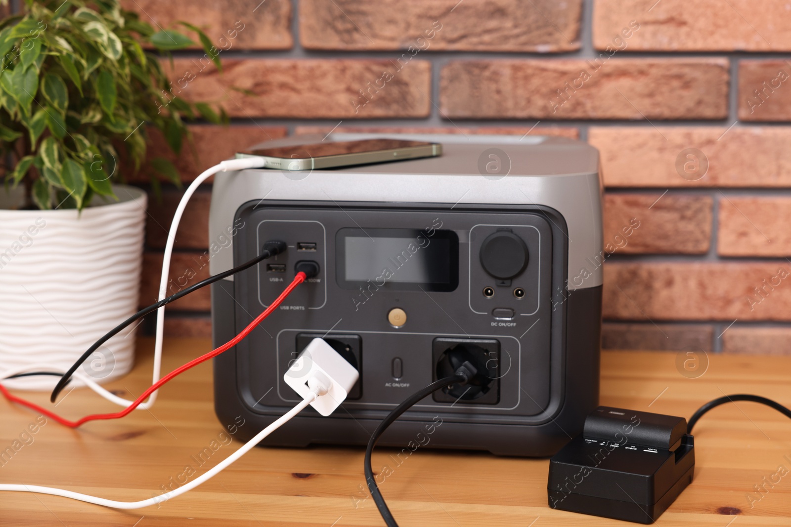 Photo of Devices charging from portable power station on wooden desk indoors