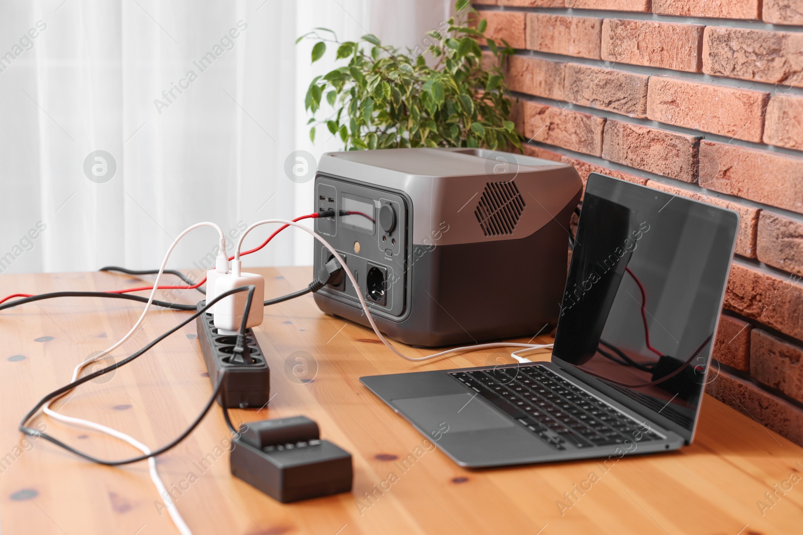 Photo of Laptop charging from portable power station on wooden desk indoors