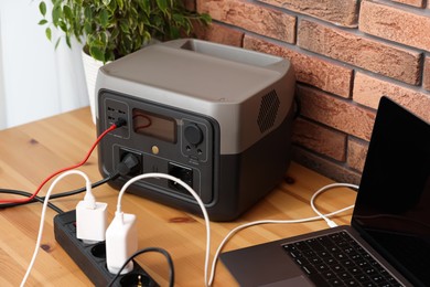 Photo of Laptop charging from portable power station on wooden desk indoors