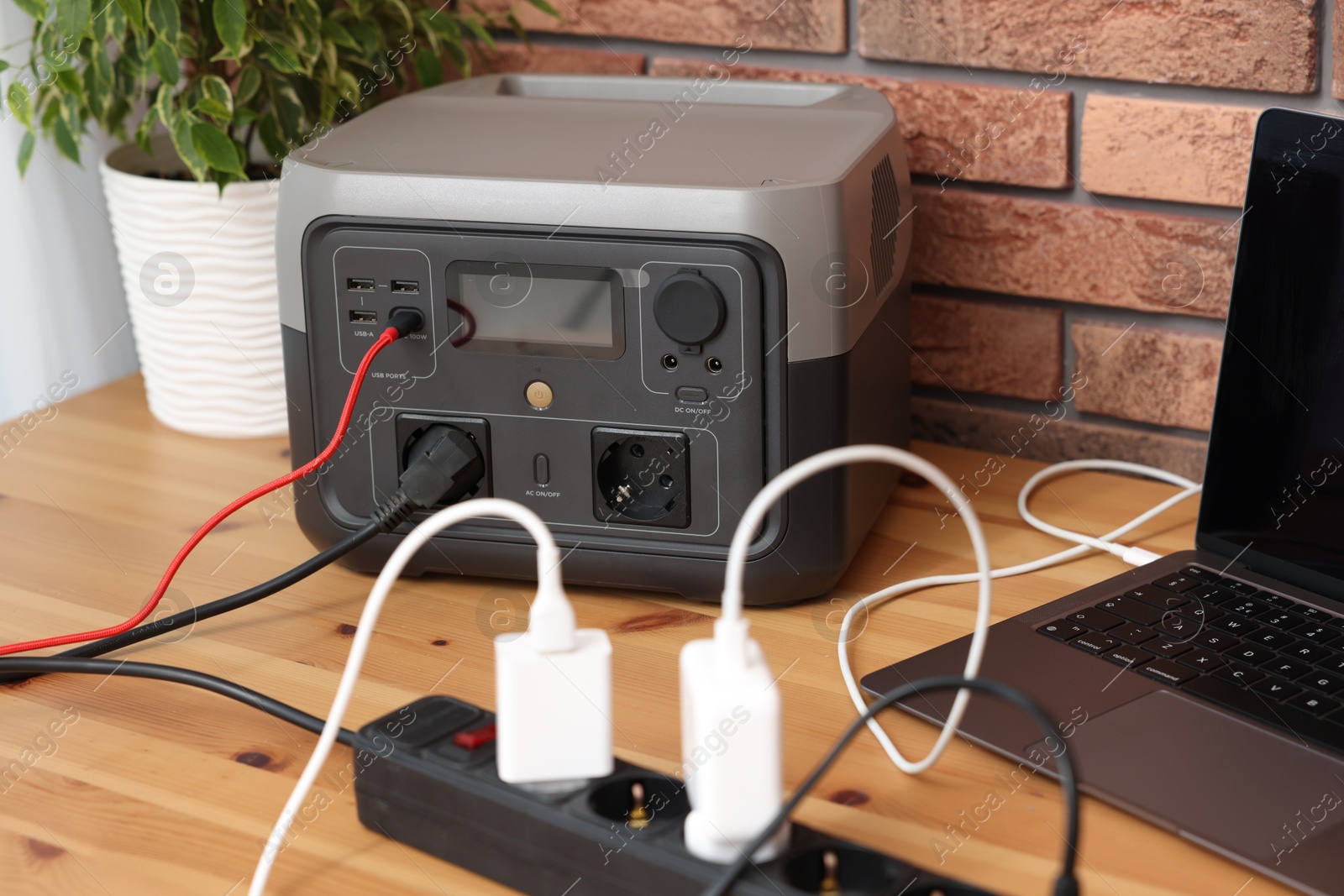 Photo of Laptop charging from portable power station on wooden desk indoors