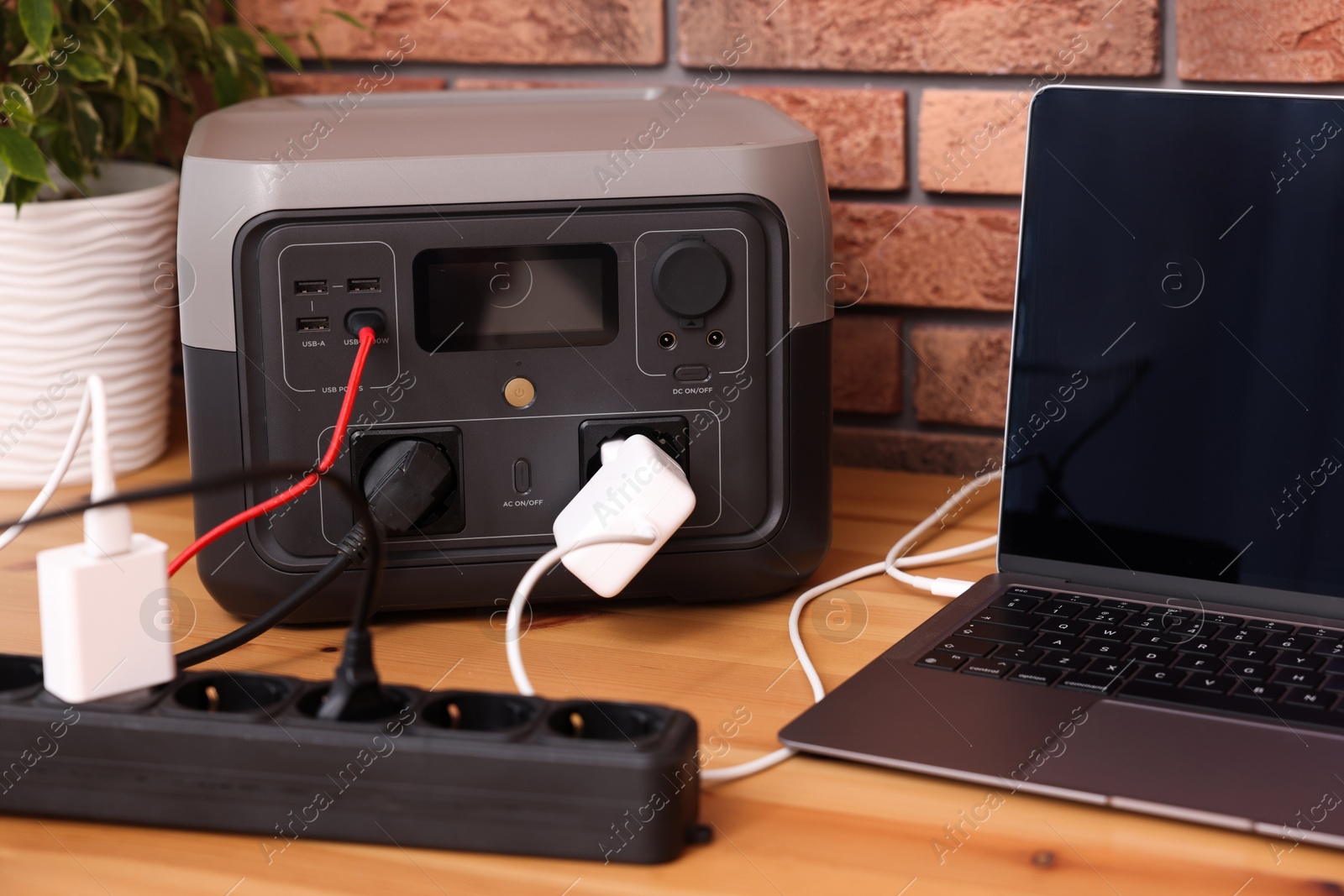 Photo of Laptop charging from portable power station on wooden desk indoors