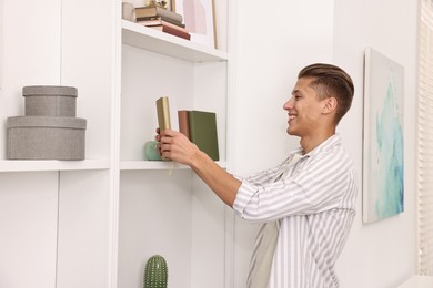 Photo of Smiling decorator arranging books onto shelf indoors