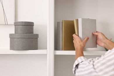 Photo of Male decorator arranging books onto shelf indoors, closeup