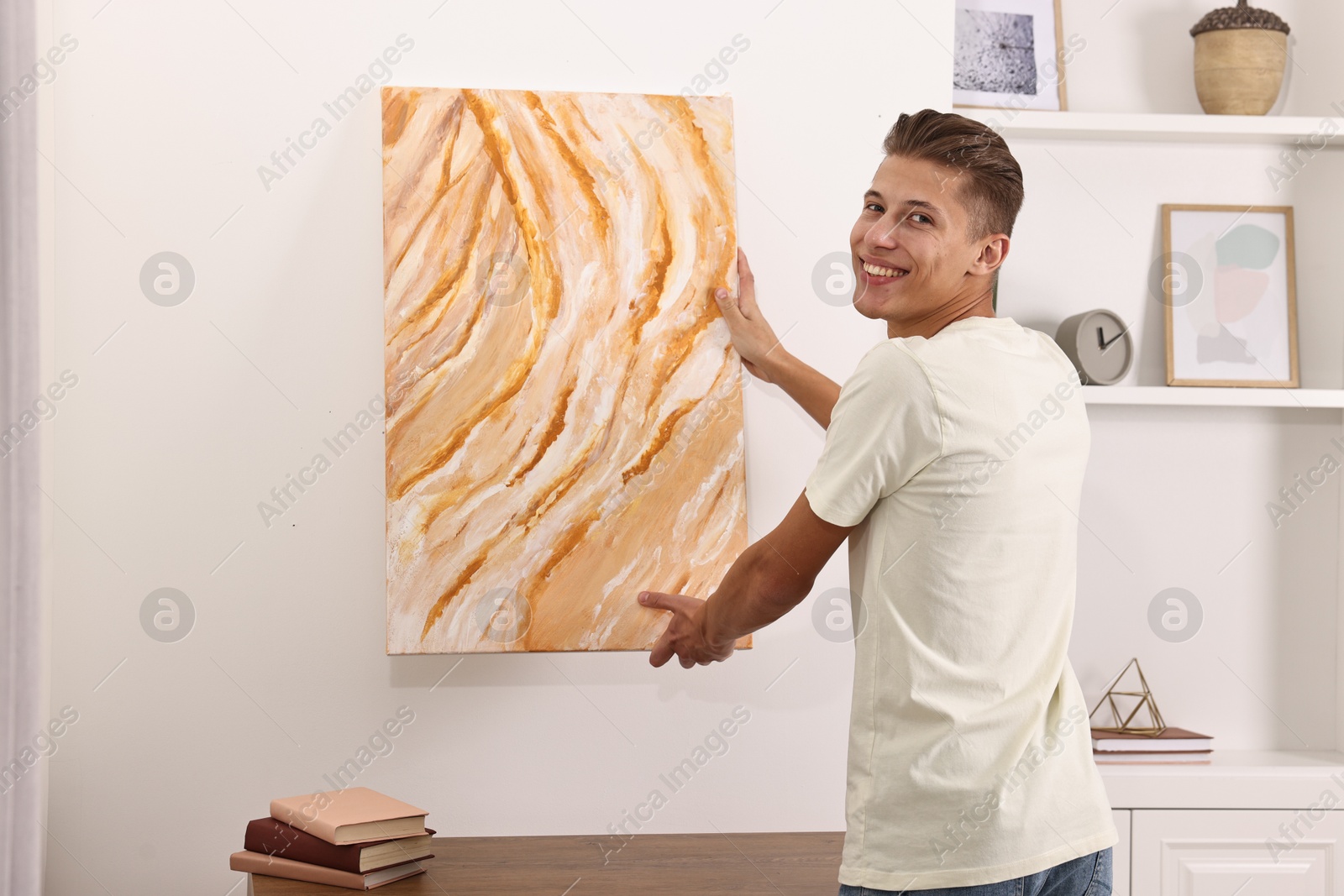 Photo of Smiling young decorator hanging abstract picture indoors