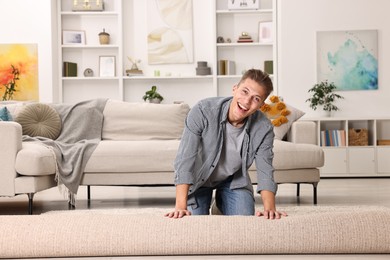 Photo of Happy decorator rolling out beige carpet indoors