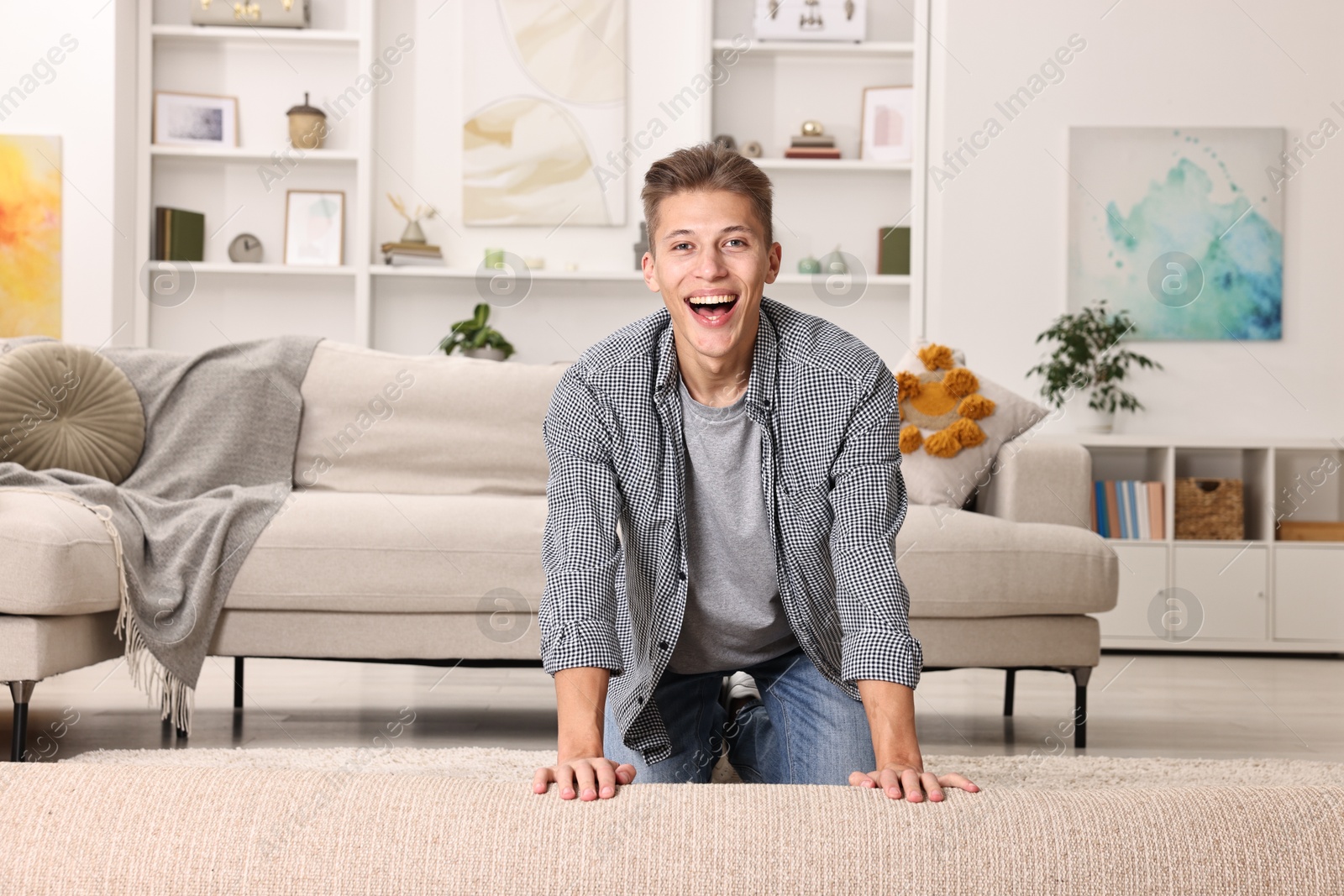 Photo of Happy decorator rolling out beige carpet indoors