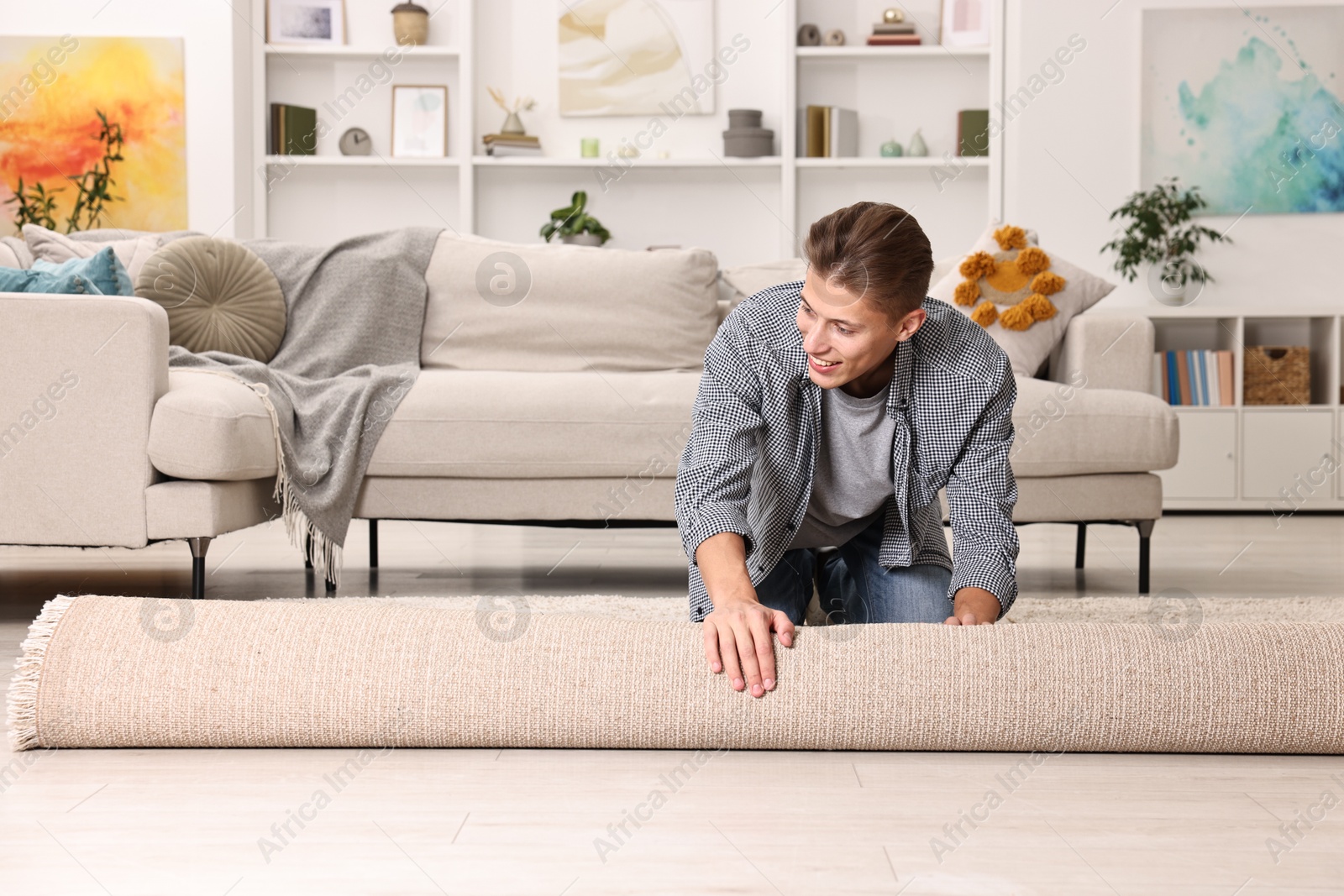 Photo of Happy decorator rolling out beige carpet indoors