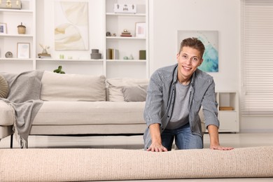 Photo of Happy decorator rolling out beige carpet indoors