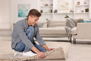 Photo of Smiling decorator placing beige carpet indoors. Space for text