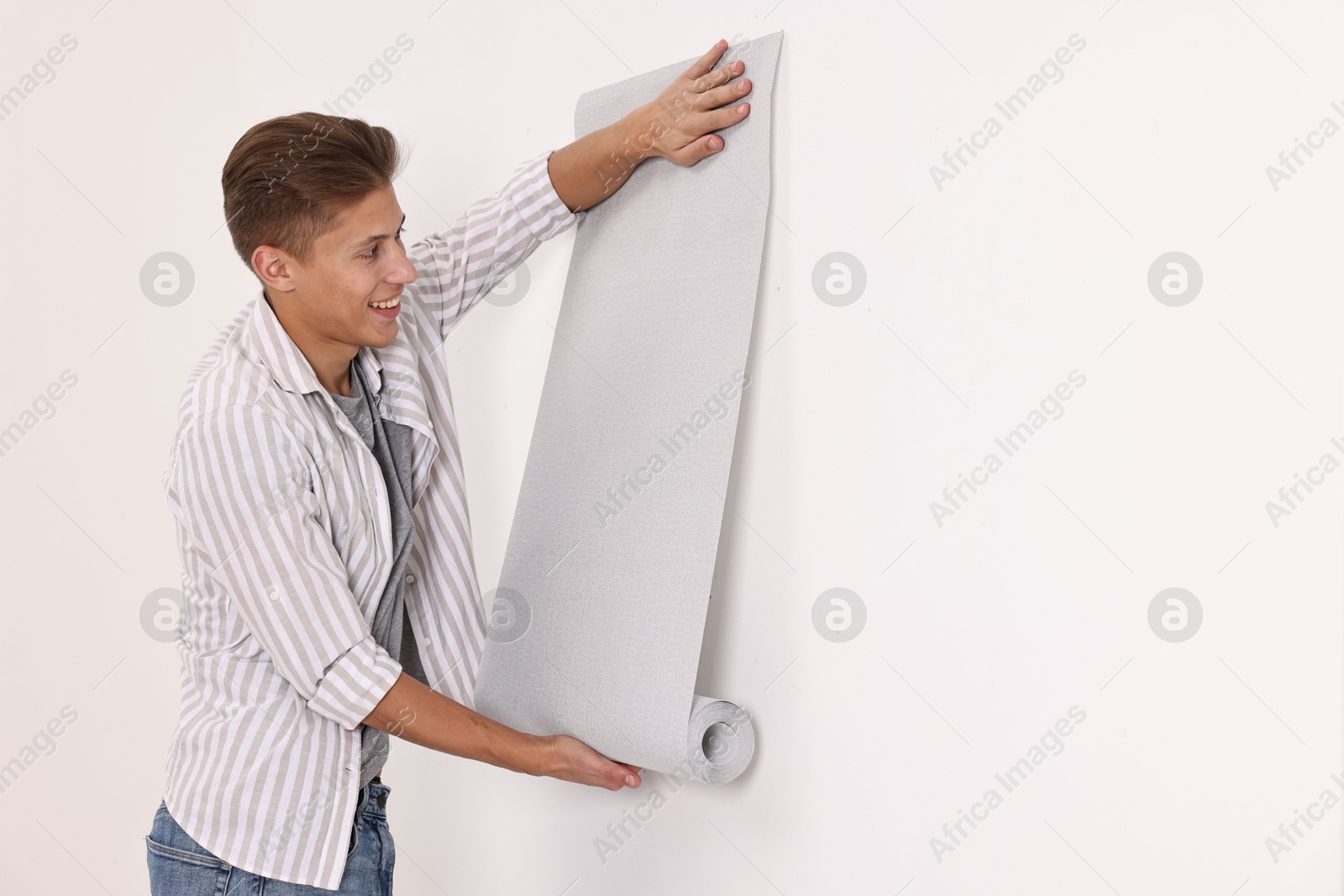 Photo of Smiling handyman hanging gray wallpaper indoors. Space for text