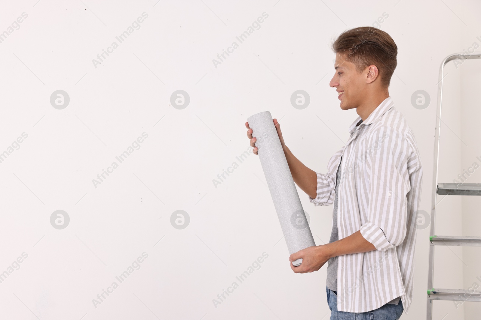 Photo of Smiling handyman with roll of wallpaper indoors. Space for text