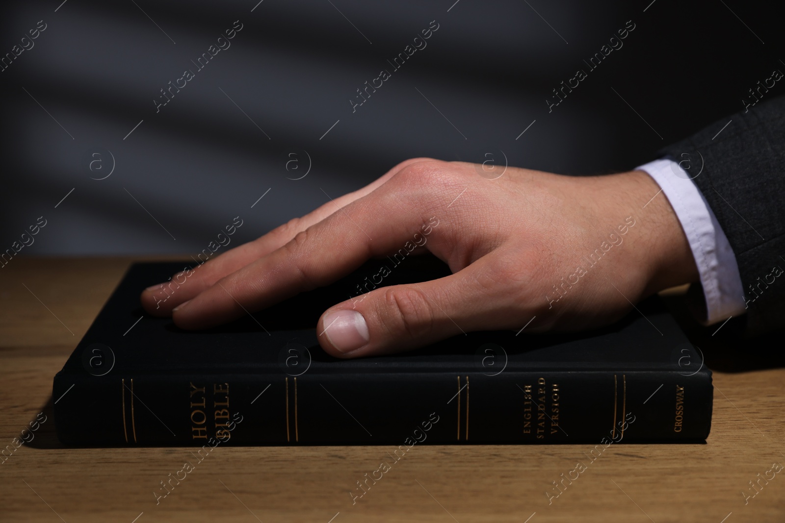 Photo of Man taking oath with his hand on Bible at wooden table, closeup