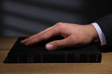 Photo of Man taking oath with his hand on Bible at wooden table, closeup