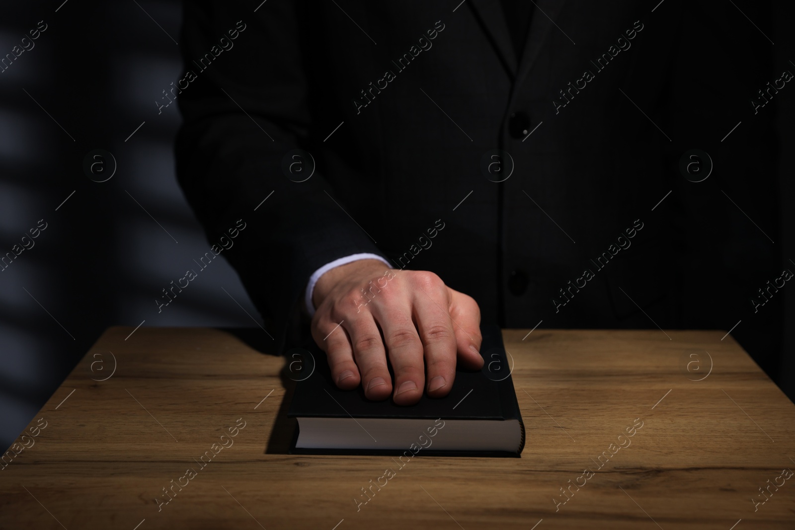 Photo of Man taking oath with his hand on Bible at wooden table, closeup