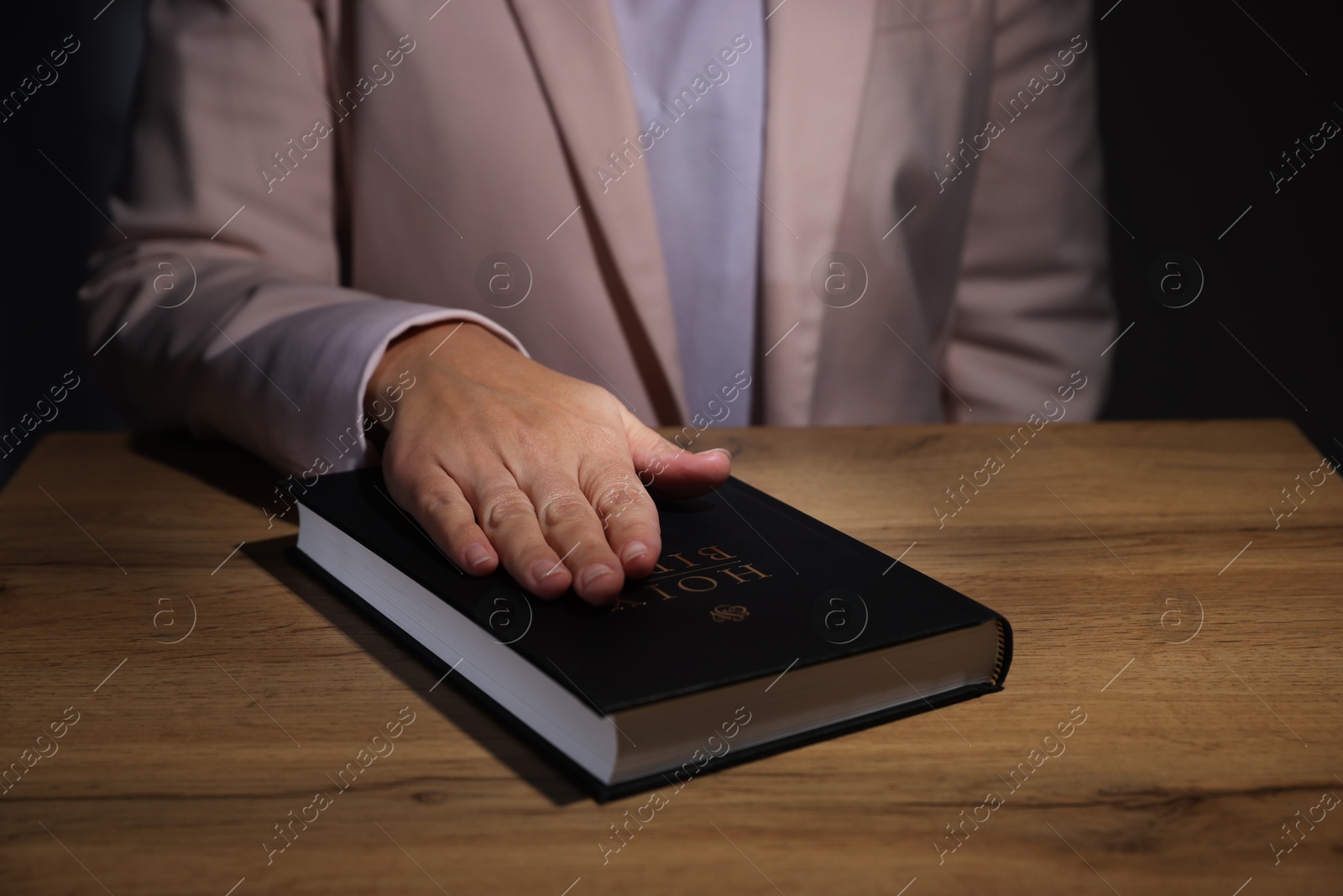 Photo of Woman taking oath with her hand on Bible at wooden table, closeup