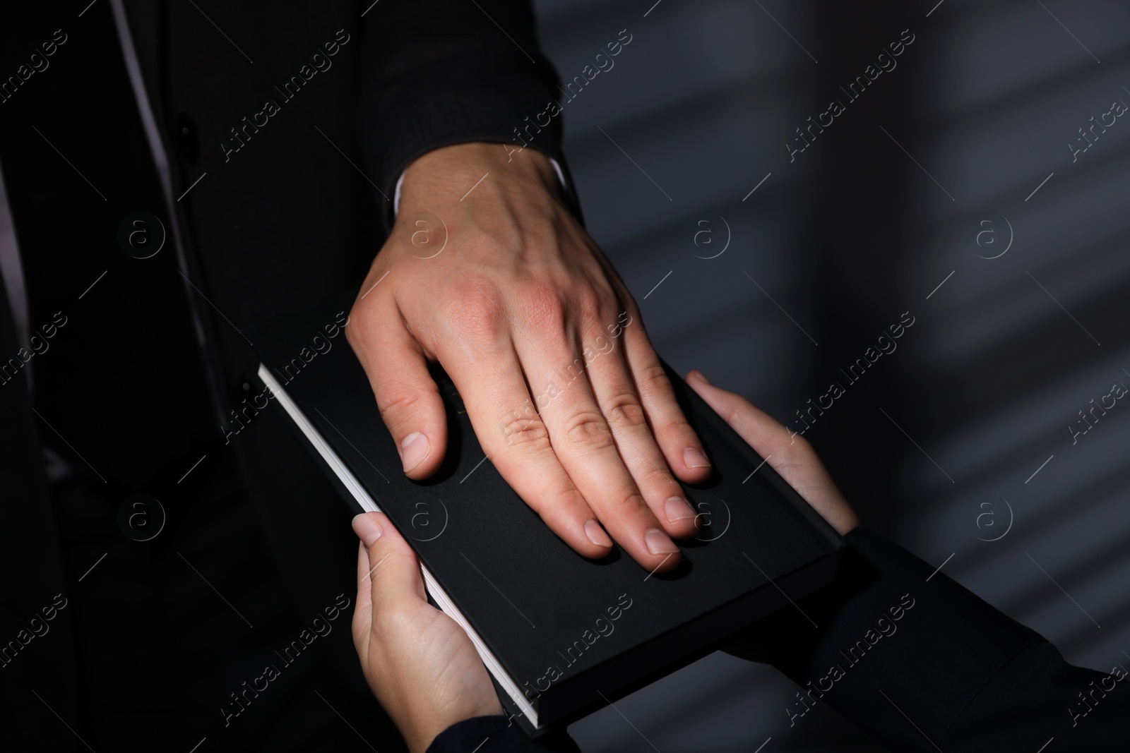 Photo of Man taking oath with his hand on Bible indoors, closeup