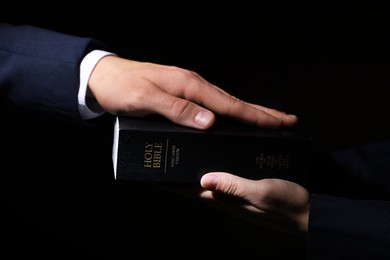 Photo of Man taking oath with his hand on Bible against black background, closeup