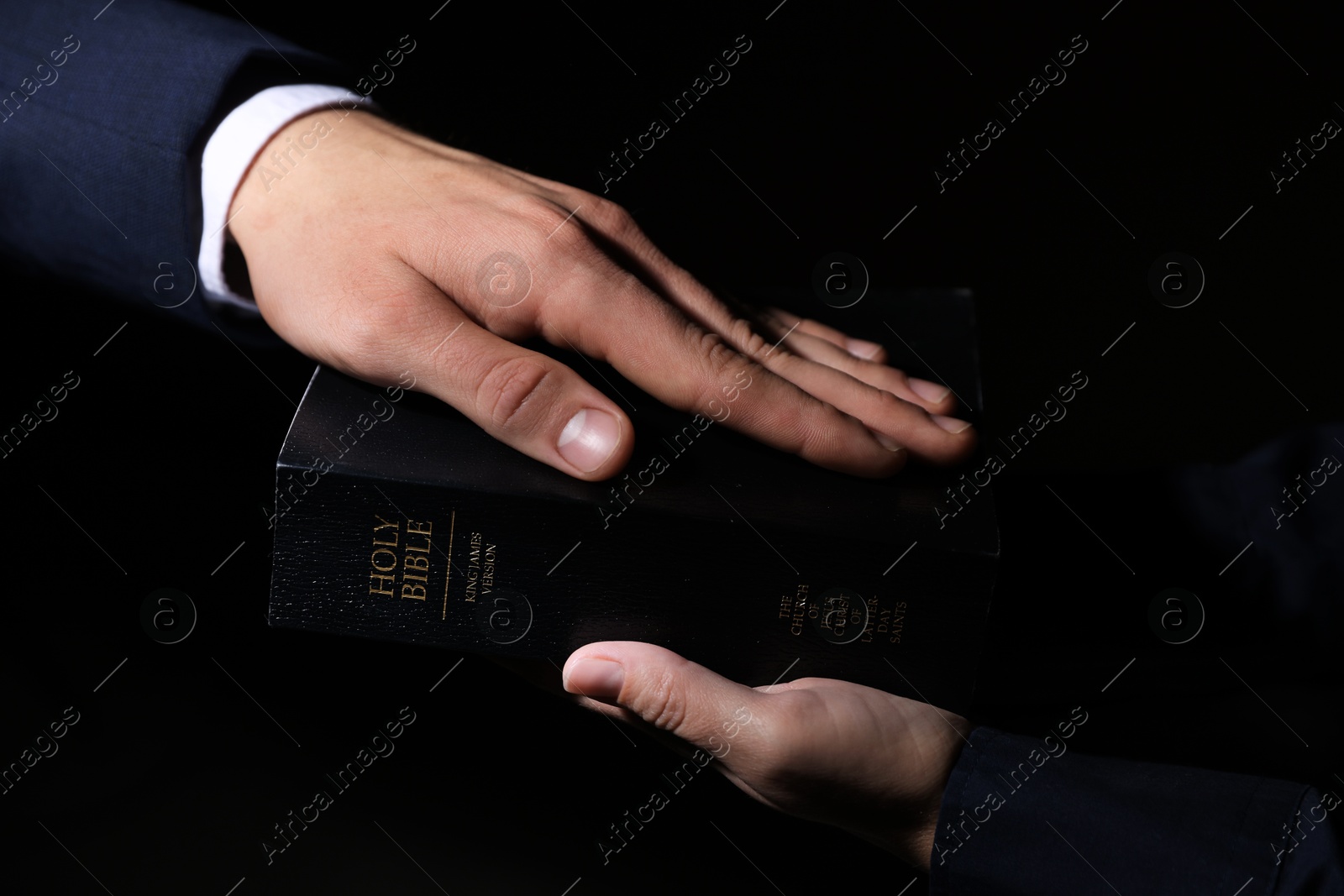 Photo of Man taking oath with his hand on Bible against black background, closeup