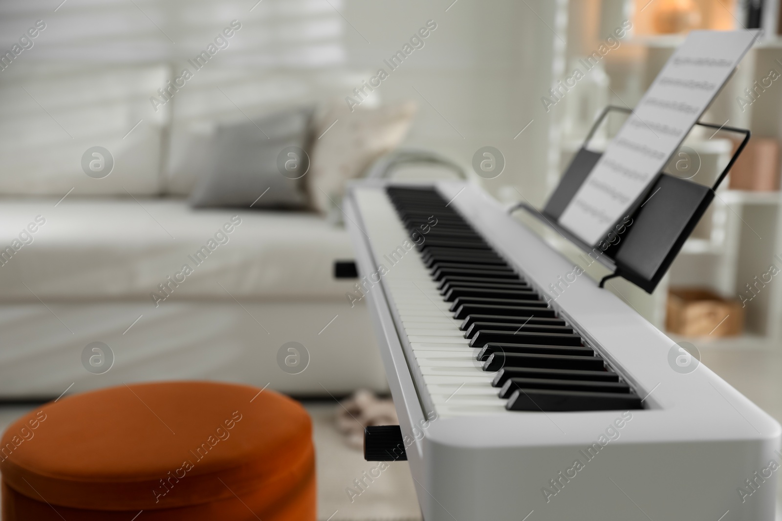 Photo of Synthesizer with music sheet and pouf at home, closeup. Space for text