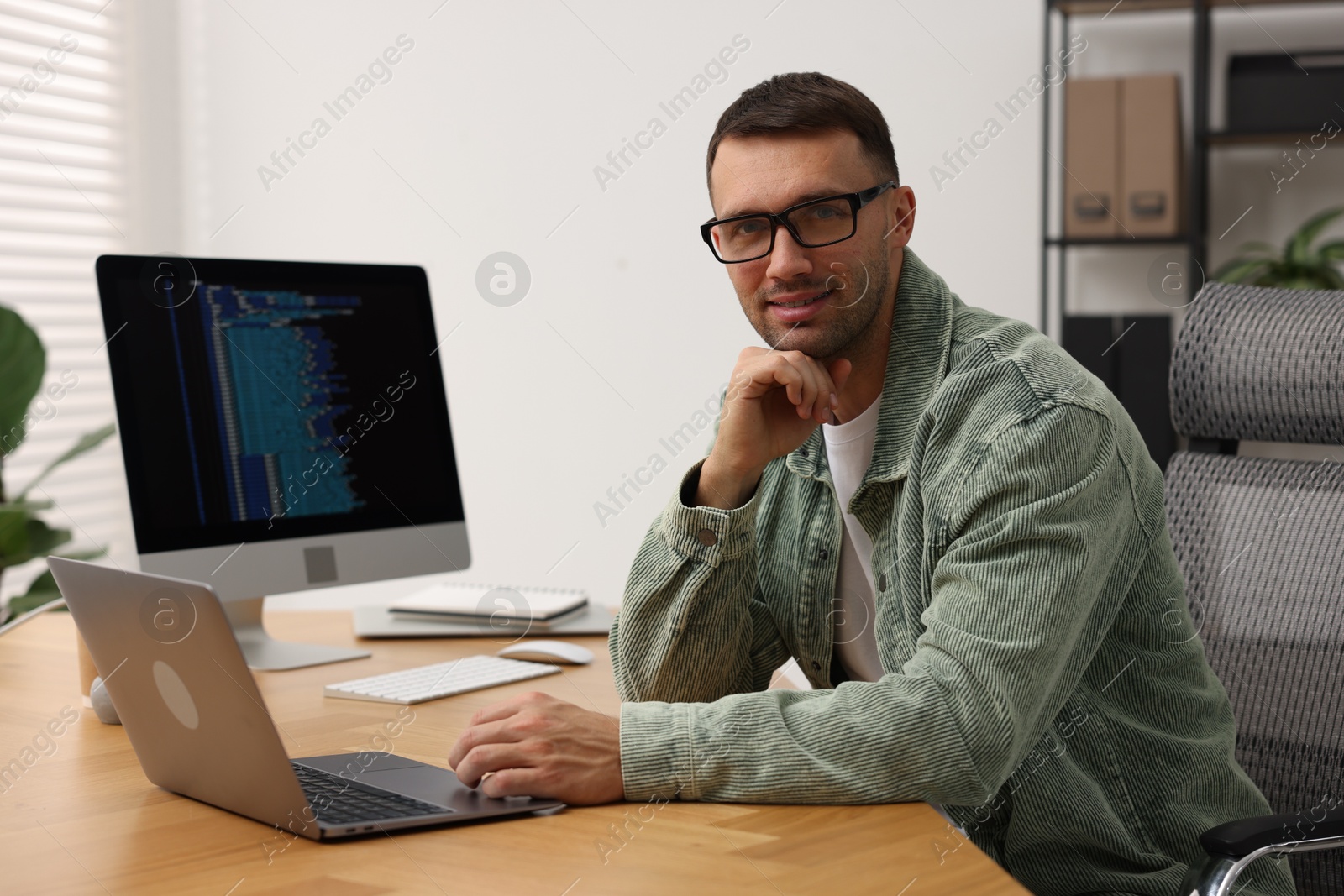 Photo of Programmer working on laptop at wooden desk indoors