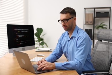 Photo of Programmer working on laptop at wooden desk indoors