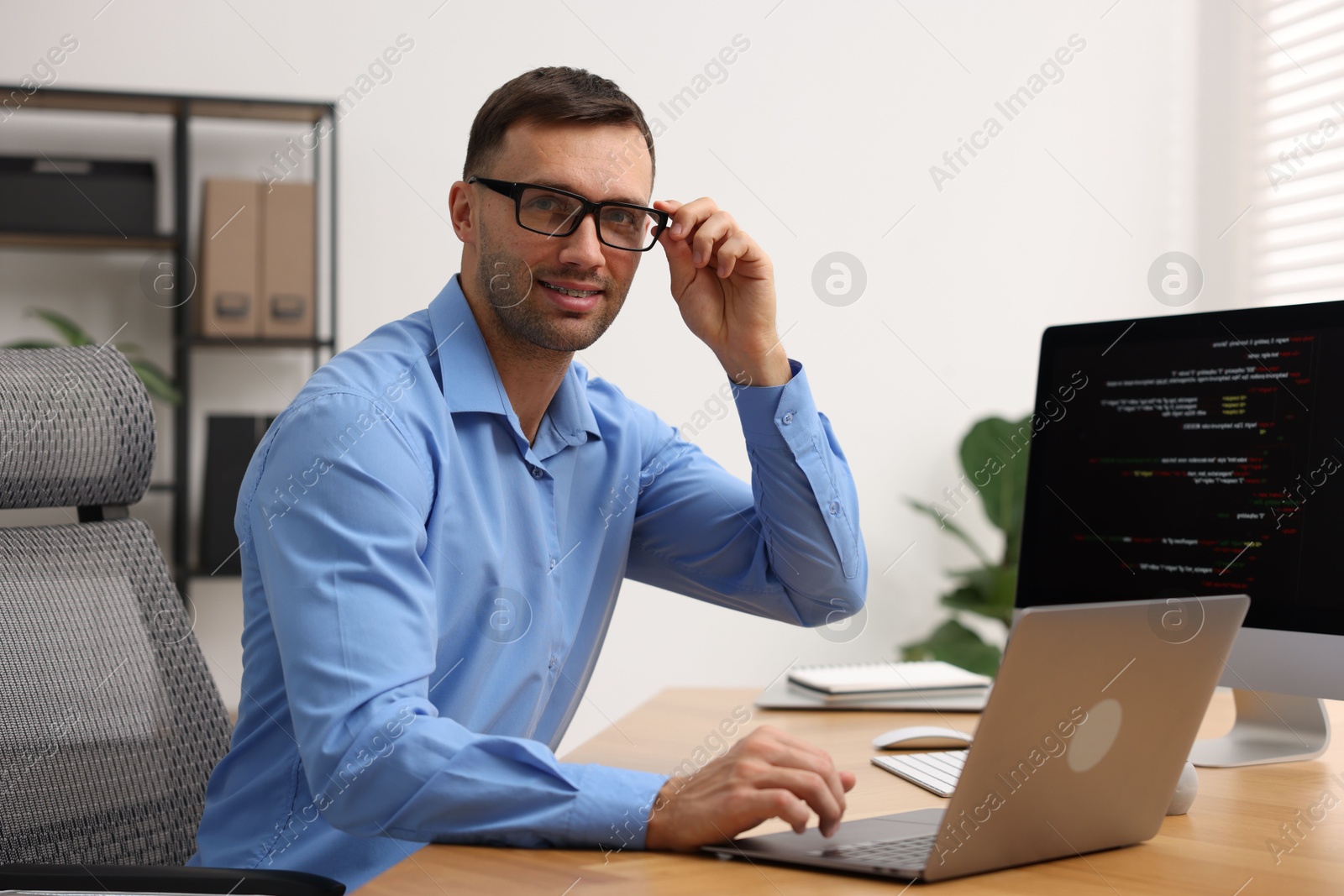 Photo of Programmer with laptop at wooden desk indoors