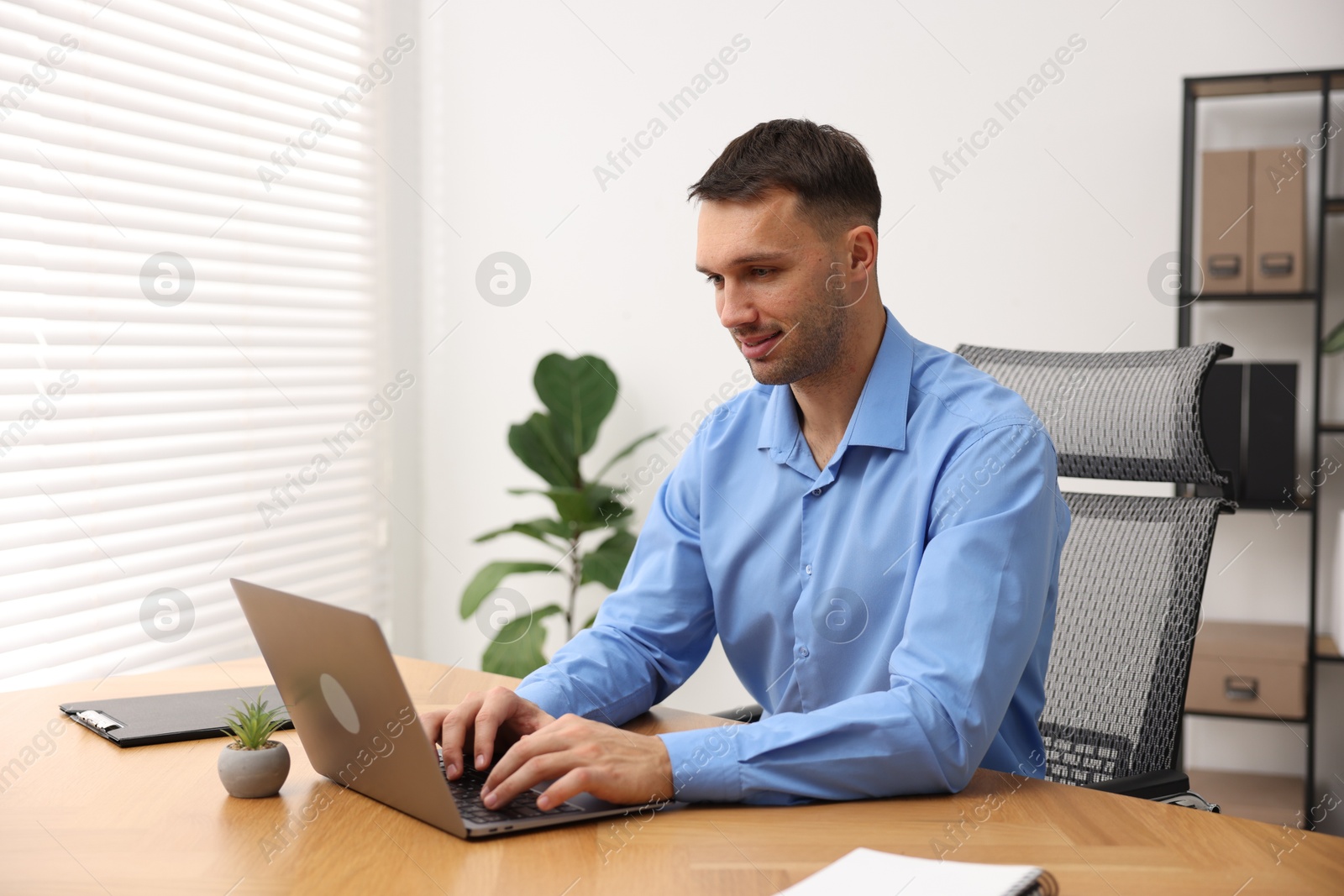 Photo of Programmer working on laptop at wooden desk indoors