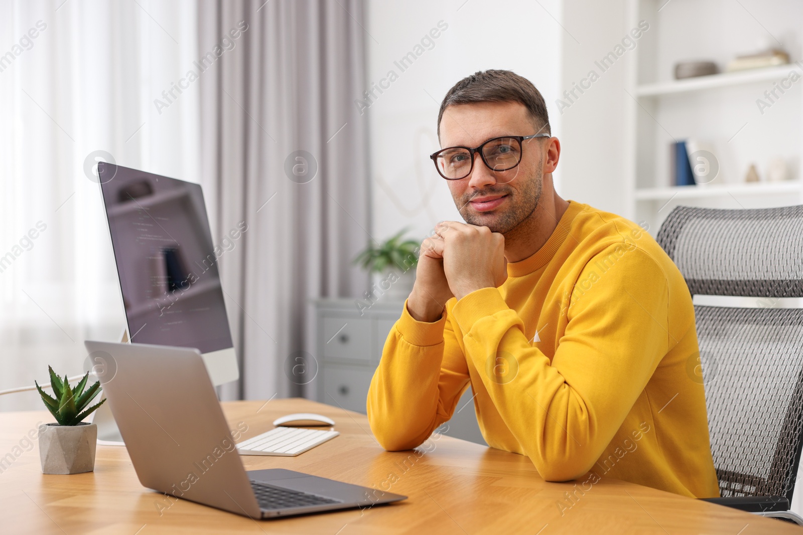 Photo of Programmer with laptop at wooden desk indoors