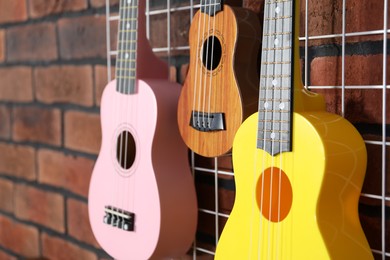 Photo of Three colorful ukulele on brick wall indoors, closeup