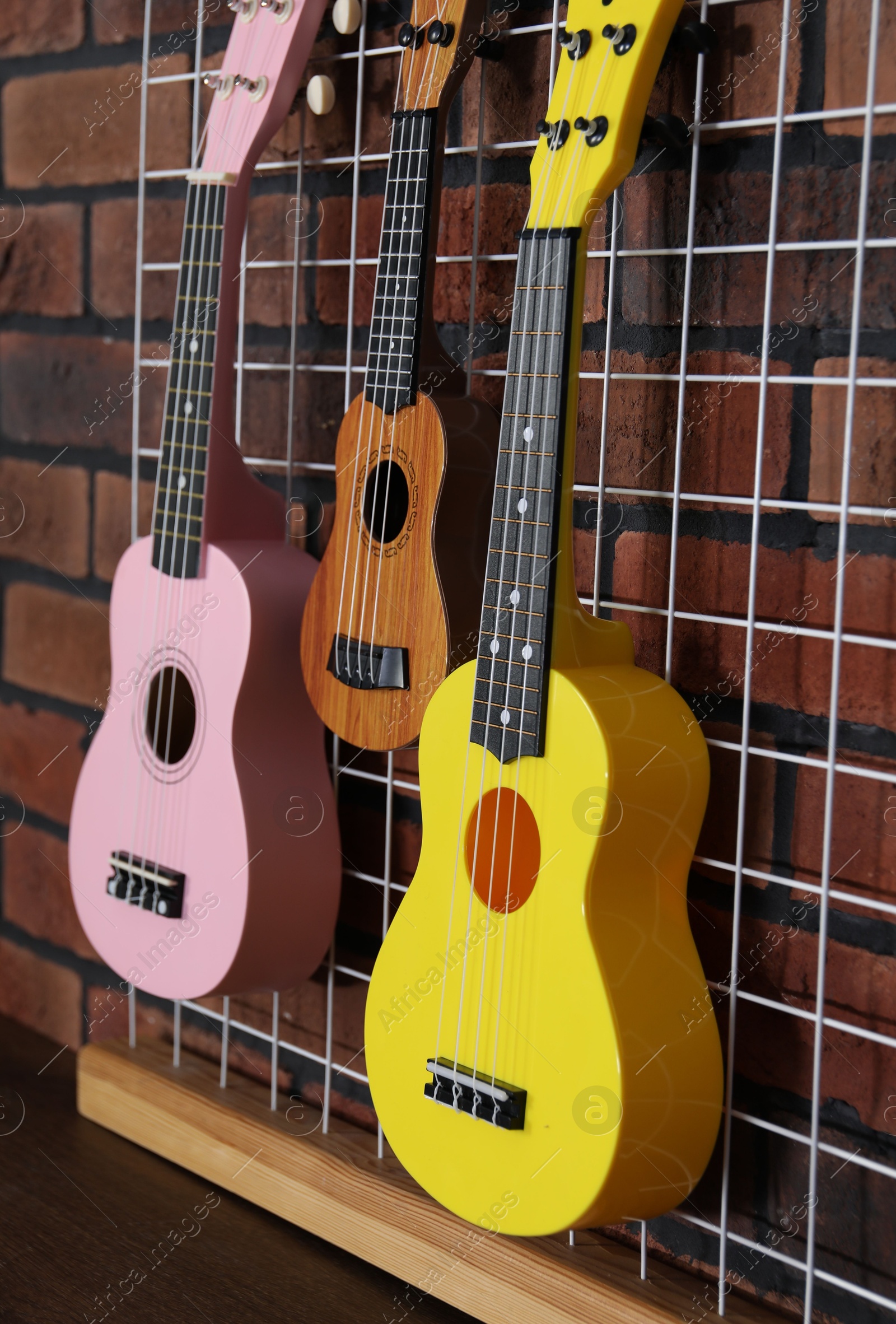 Photo of Three colorful ukulele on brick wall indoors