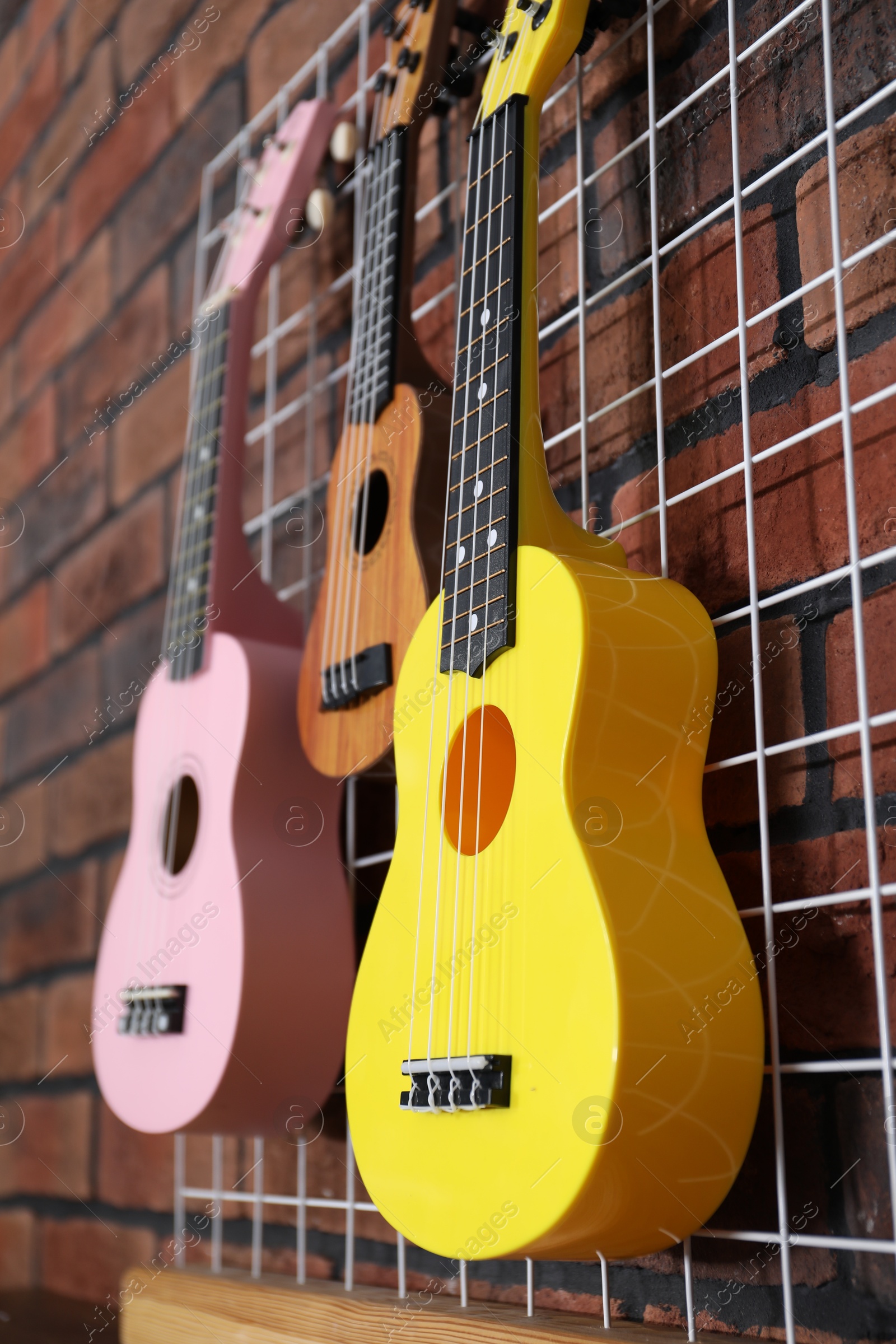 Photo of Three colorful ukulele on brick wall indoors