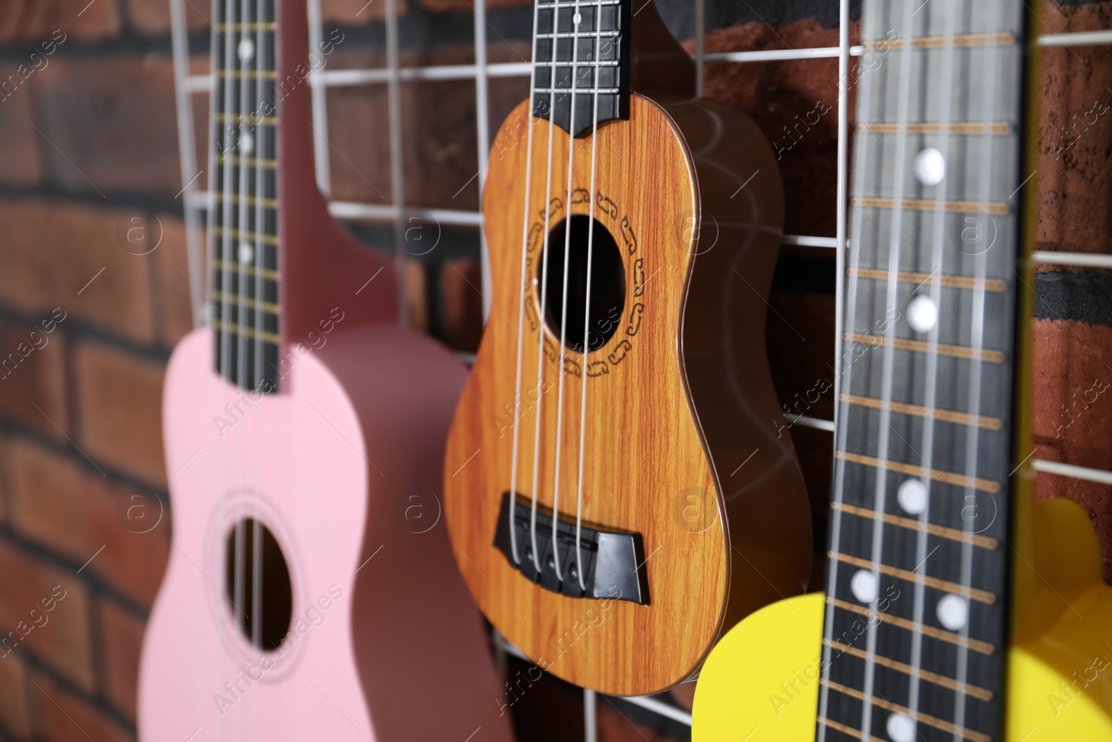 Photo of Three colorful ukulele on brick wall indoors, closeup