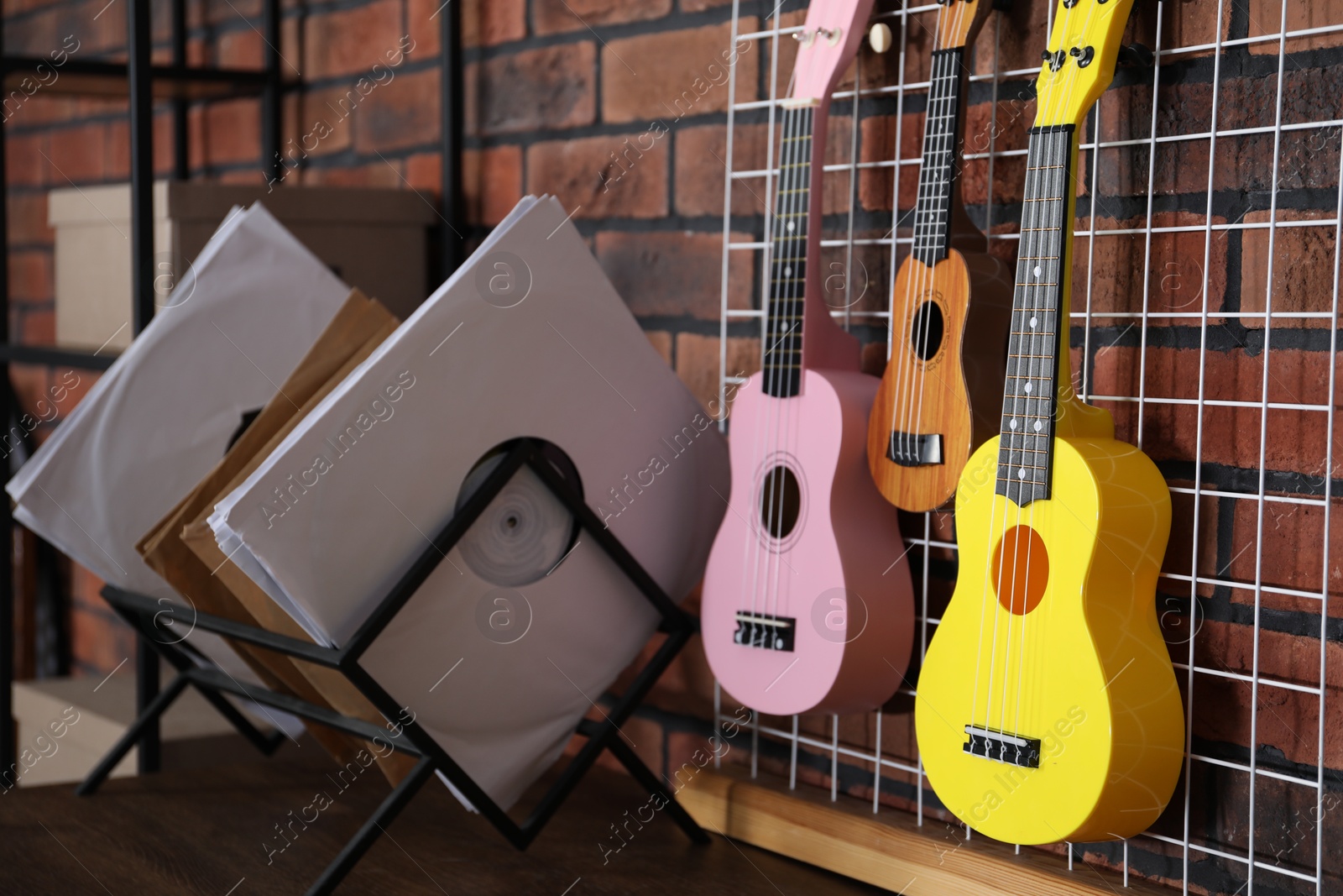 Photo of Three colorful ukulele on brick wall and records indoors