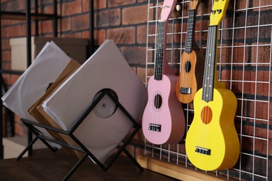 Photo of Three colorful ukulele on brick wall and records indoors