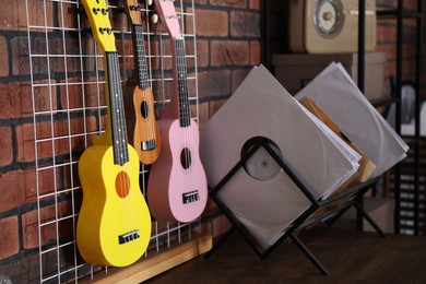 Photo of Three colorful ukulele on brick wall and records indoors