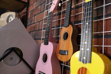 Photo of Three colorful ukulele on brick wall and records indoors, closeup