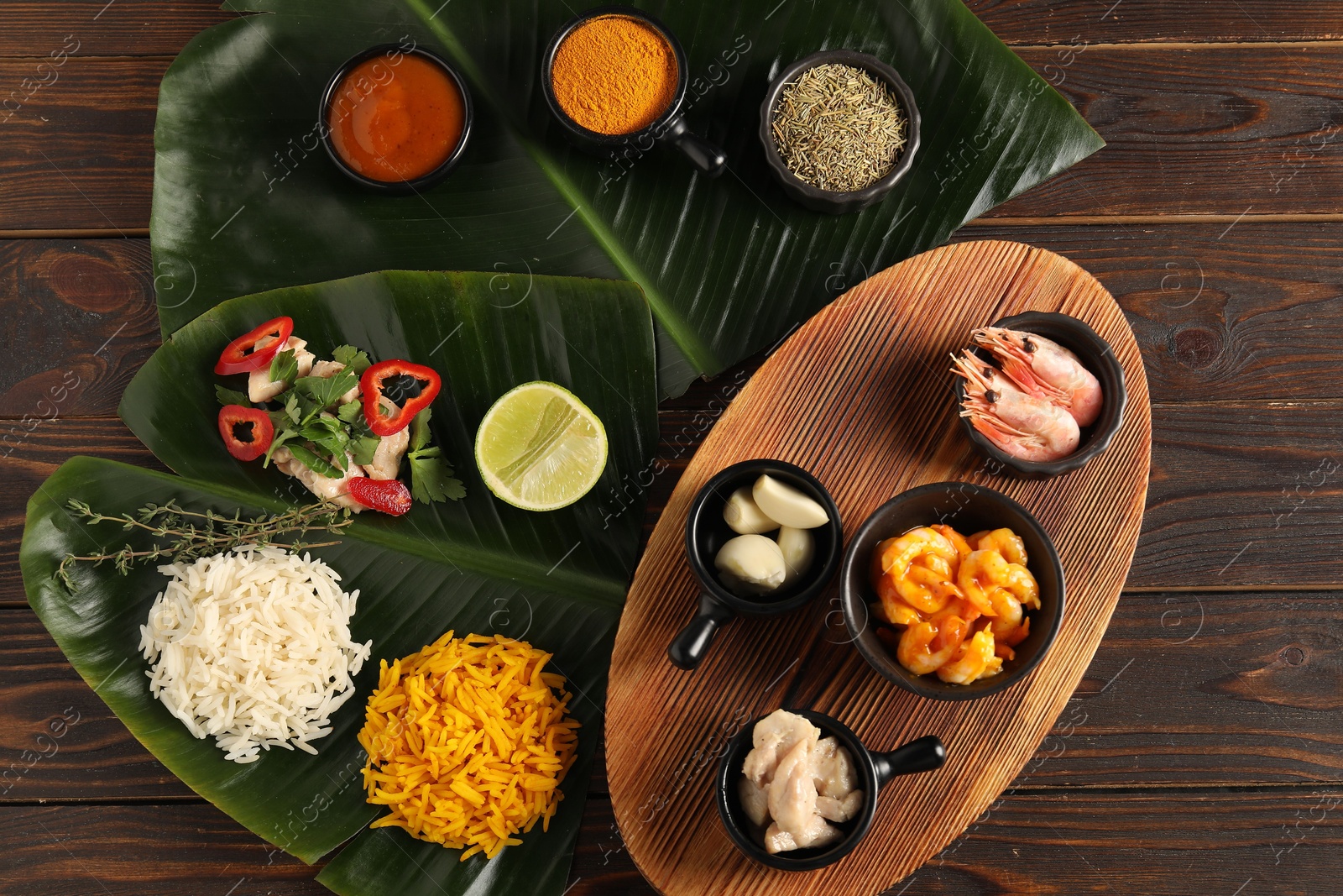 Photo of Cut banana leaves with different food, board, spices and sauce on wooden table, flat lay