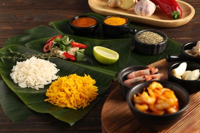 Photo of Cut banana leaves with different food, board, spices and sauce on wooden table, closeup