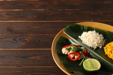 Photo of Cut banana leaf with different food on wooden table. Space for text