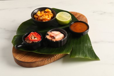 Photo of Cut banana leaf with different food and sauce on white marble table, closeup