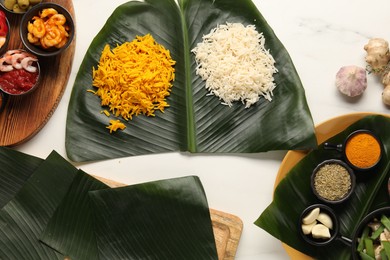 Photo of Cut banana leaves with different food, spices and sauce on white table, flat lay