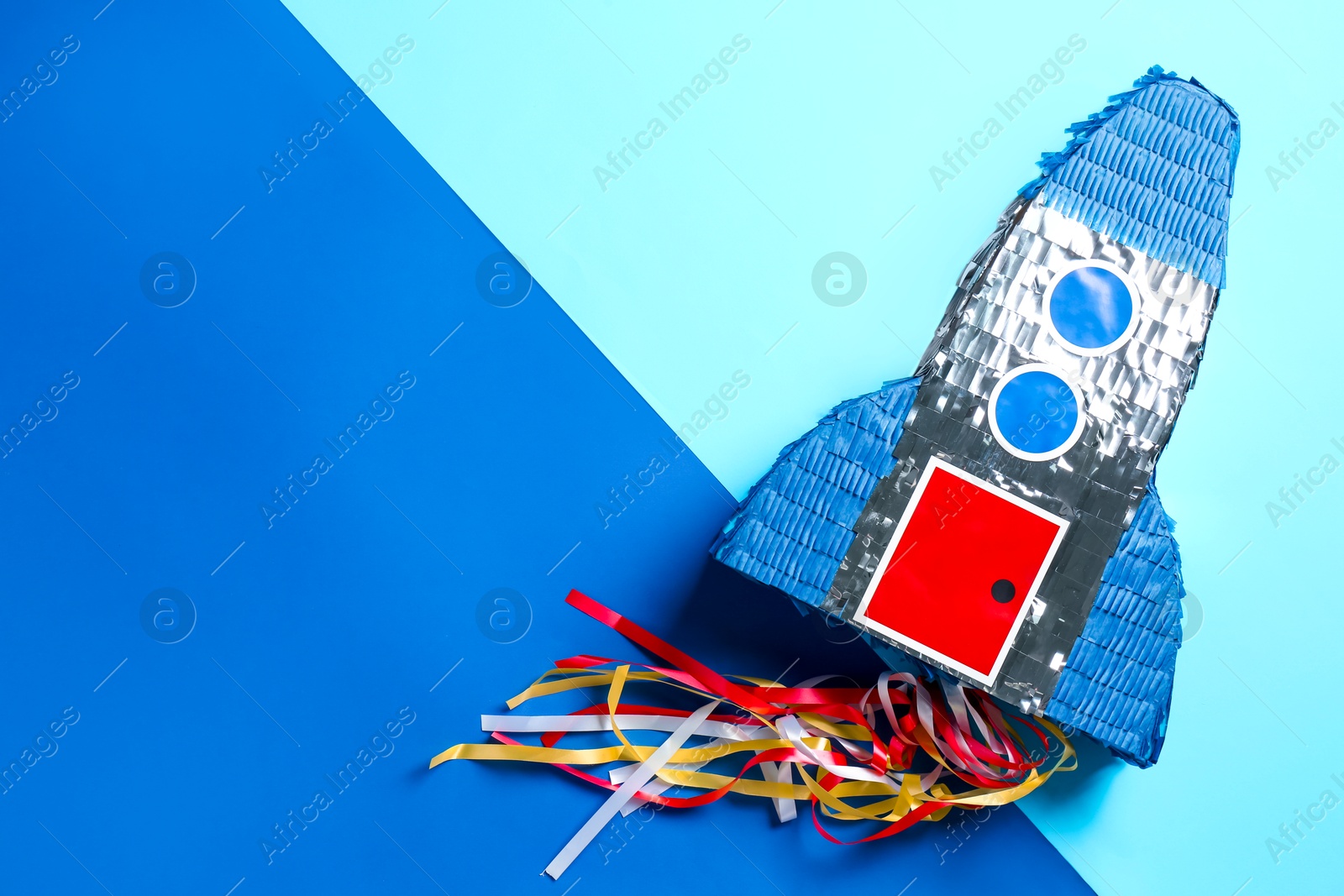 Photo of Bright pinata in shape of spaceship on blue background, top view. Space for text