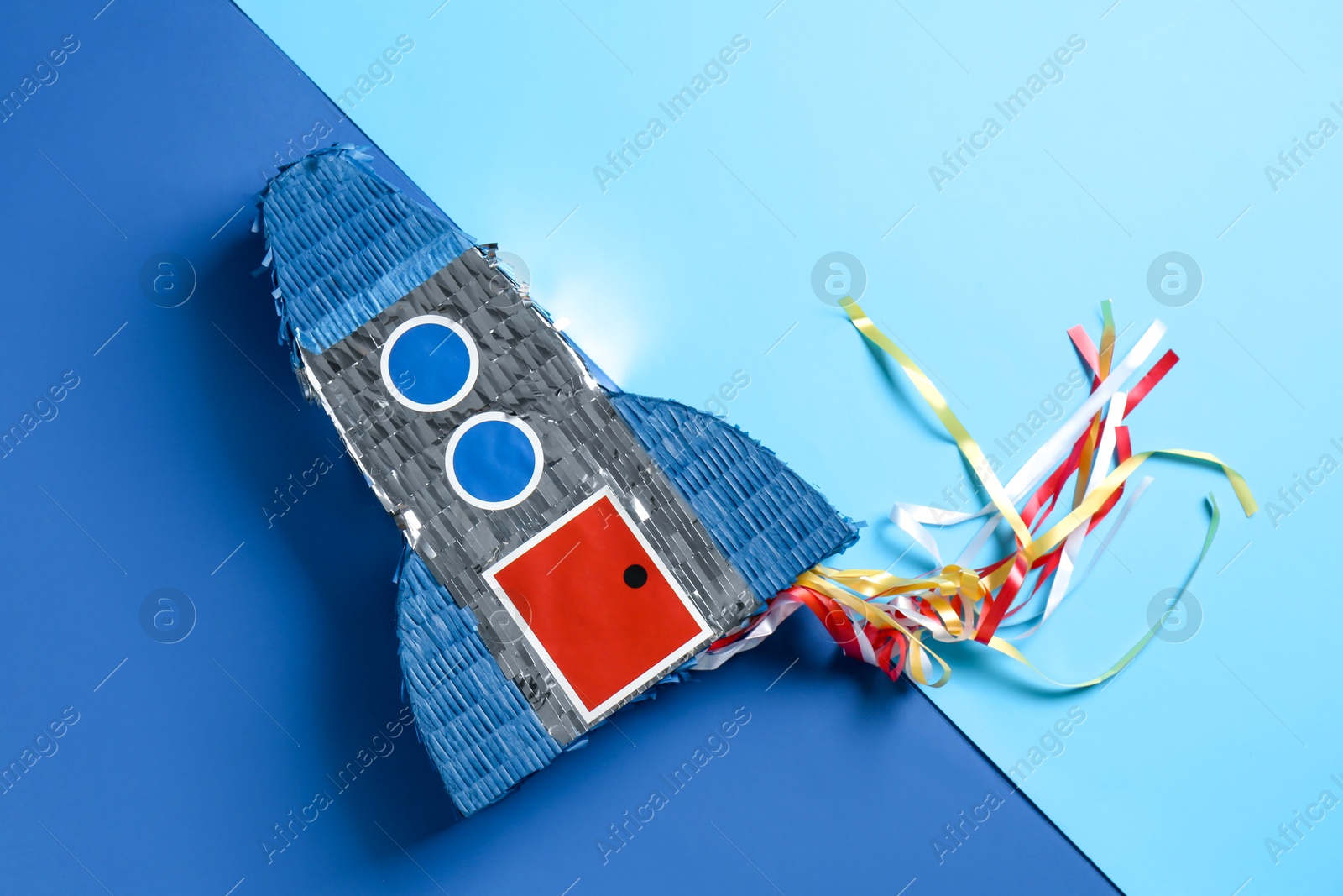 Photo of Bright pinata in shape of spaceship on blue background, top view