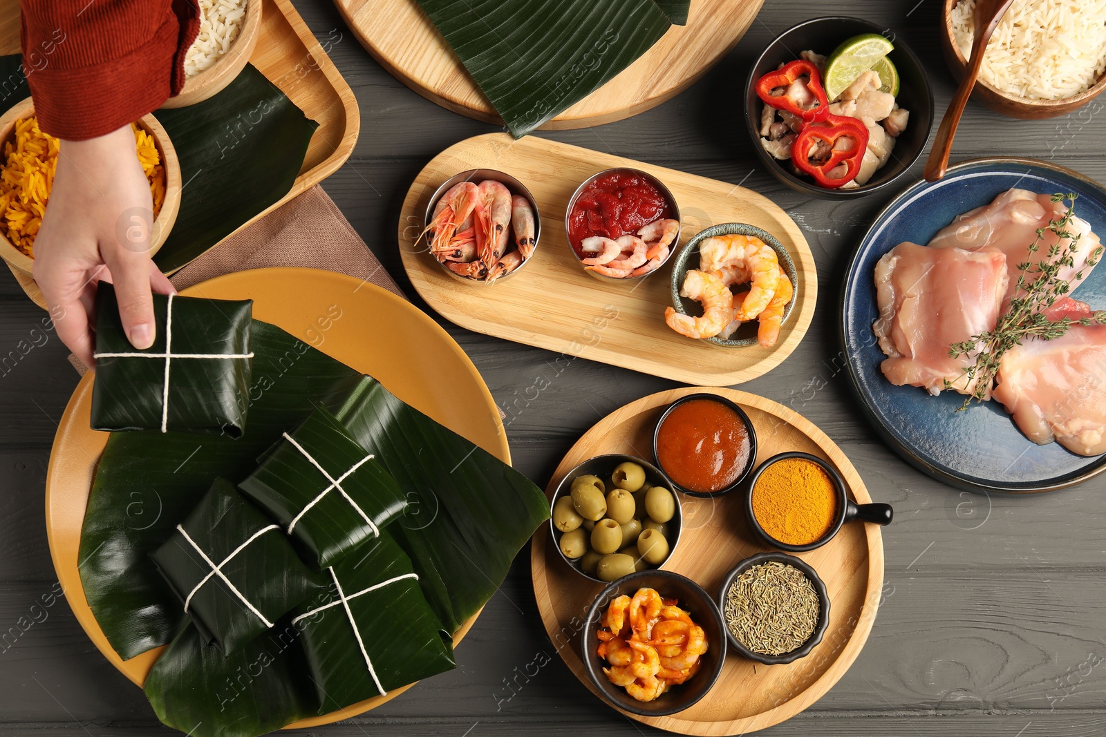 Photo of Woman taking folded banana leaf with food at wooden table with products, top view