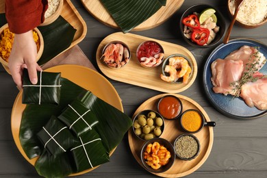 Photo of Woman taking folded banana leaf with food at wooden table with products, top view