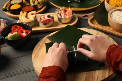 Photo of Woman tying banana leaf with food at wooden table with products, closeup. Healthy eco serving