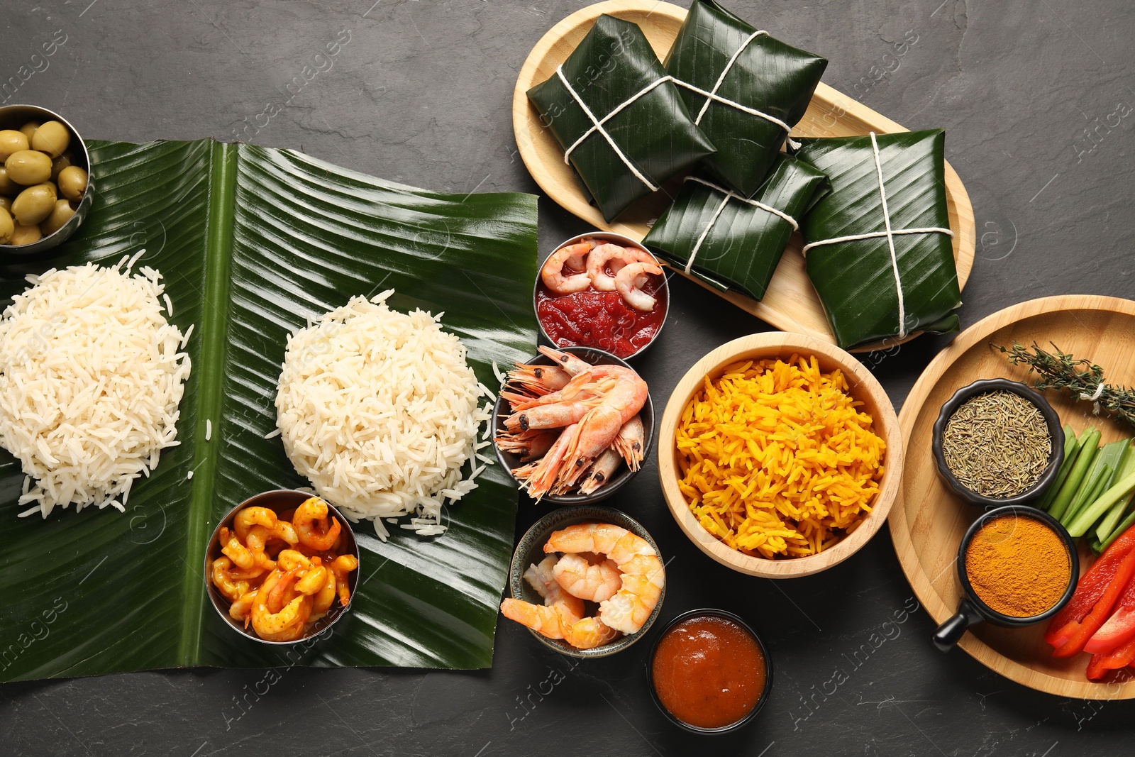 Photo of Cut banana leaves with different food, spices and sauce on dark textured table, flat lay. Healthy eco serving