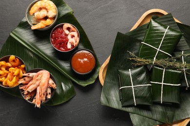 Photo of Cut banana leaves with different food, spices and sauce on dark textured table, flat lay. Healthy eco serving