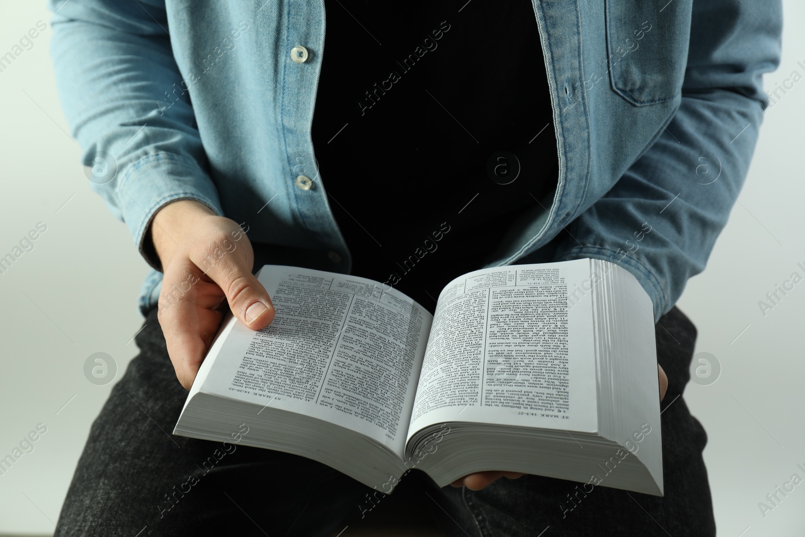 Photo of Man reading Holy Bible in English language on light background, closeup